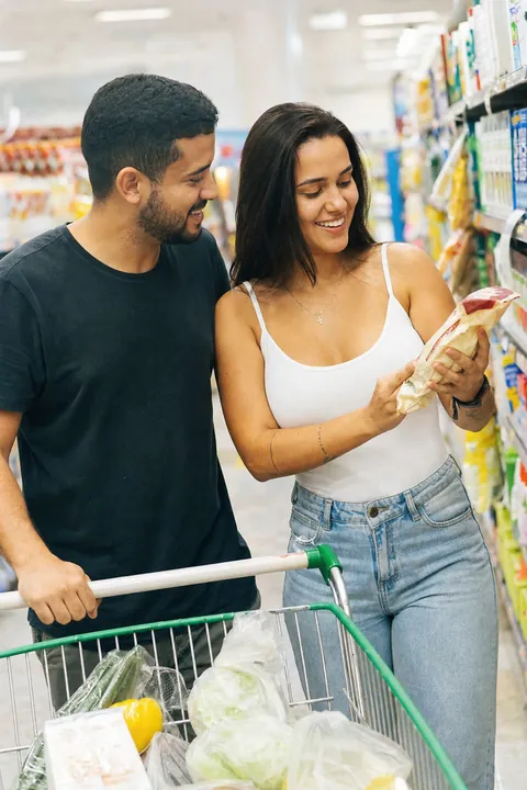 Casal fazendo compras no supermercado, ela mostra um rótulo para ele