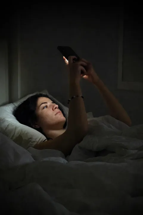 Mulher deitada no escuro, iluminada só pela tela do celular