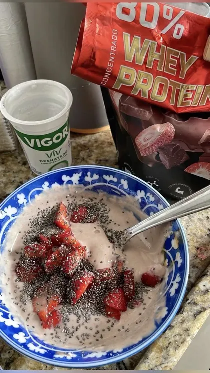 Tigela de iogurte com morango e chia, whey e copo de iogurte na bancada
